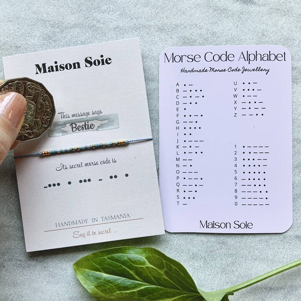 Morse Code Bracelet mounted on a display card. A scratch and reveal panel has been removed to display the word 'Bestie'. The beads are arranged on the bracelet using Morse Code to spell out the word.