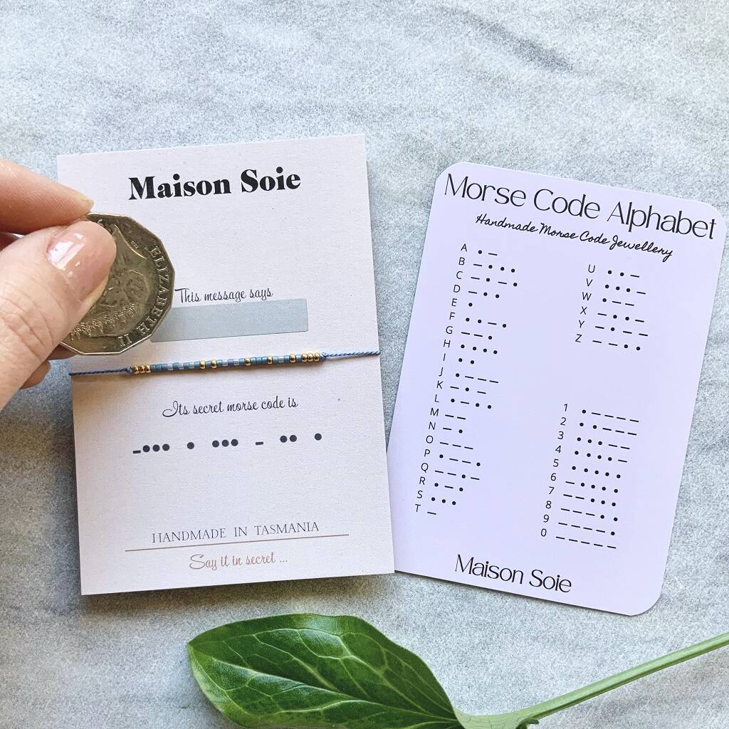 Morse Code Bracelet mounted on a display card. A scratch and reveal panel hides the secret word and is about to be revealed using a coin.