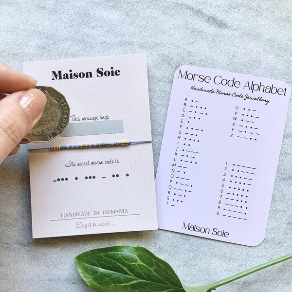 Morse Code Bracelet mounted on a display card. A scratch and reveal panel hides the secret word and is about to be revealed using a coin.